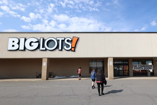 Shoppers entering a bright discount store with reopening banners